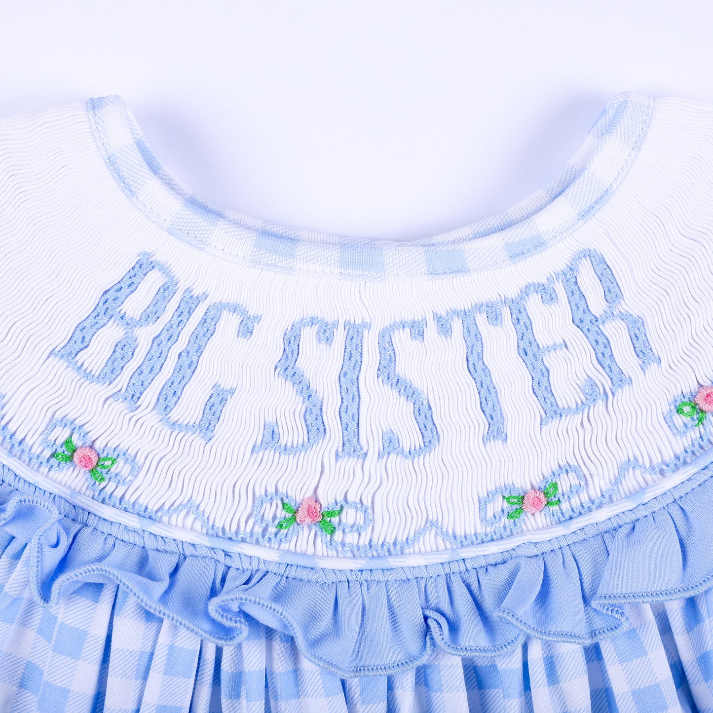Macro view of hand-smocked Big Sister embroidery with delicate floral accents and blue ruffled collar.