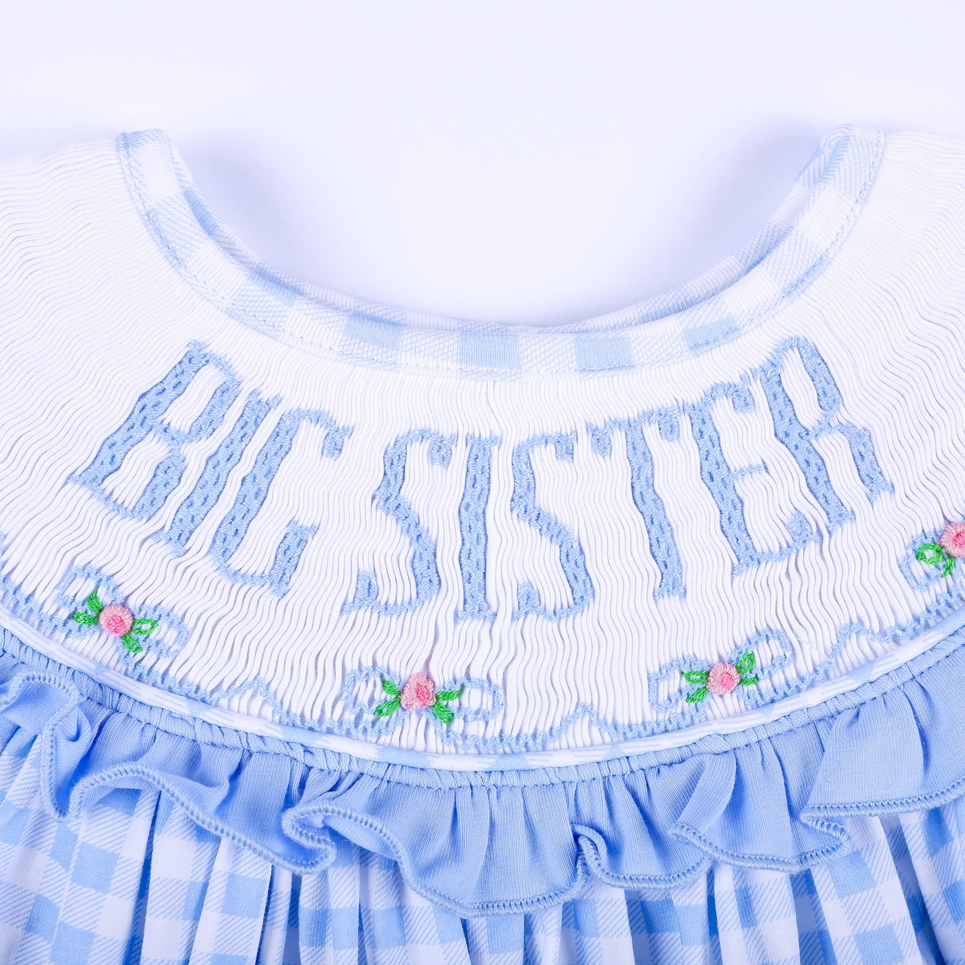 Macro view of hand-smocked Big Sister embroidery with delicate floral accents and blue ruffled collar.