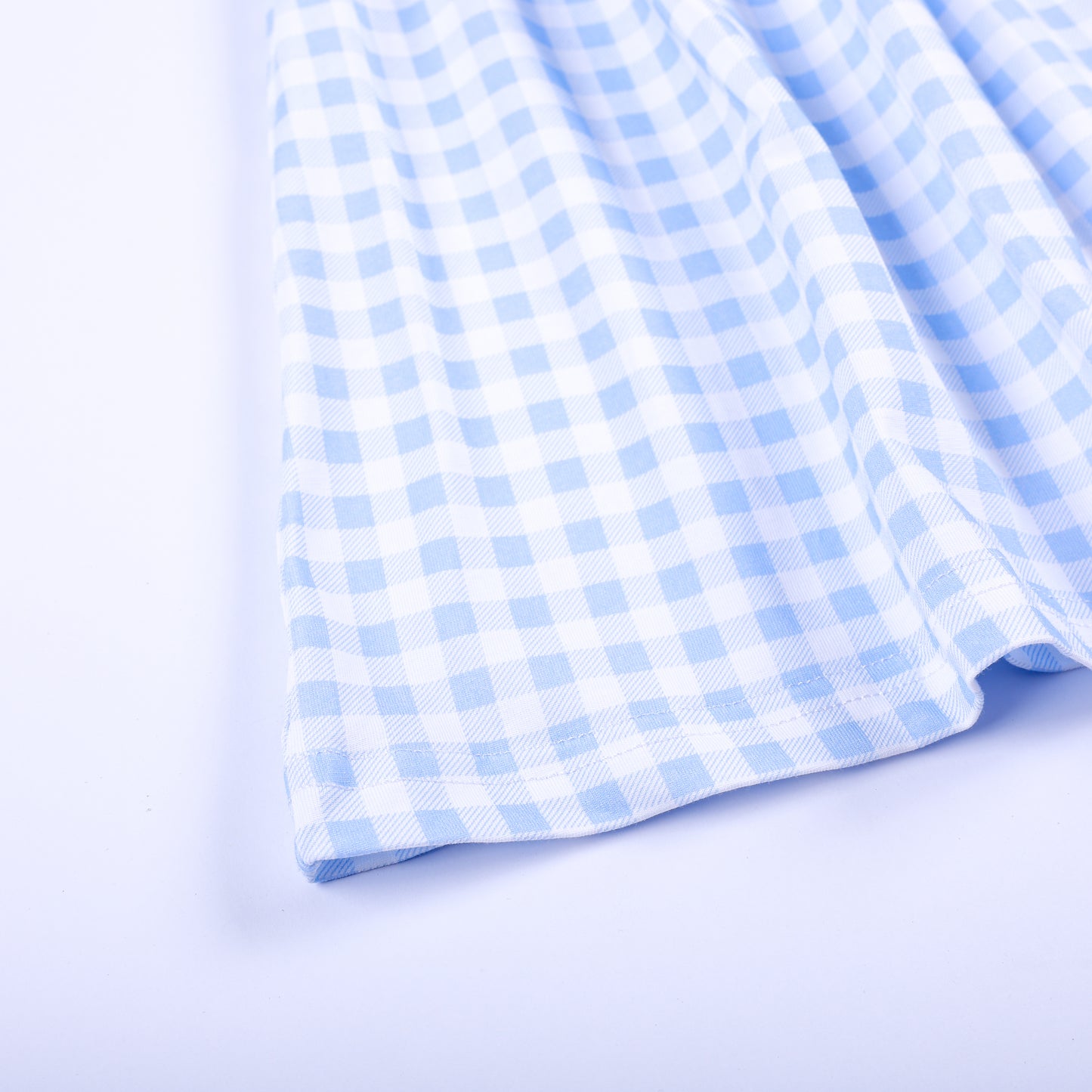 Close-up view of the light blue and white gingham woven fabric hem on a boutique hand-smocked girls dress.