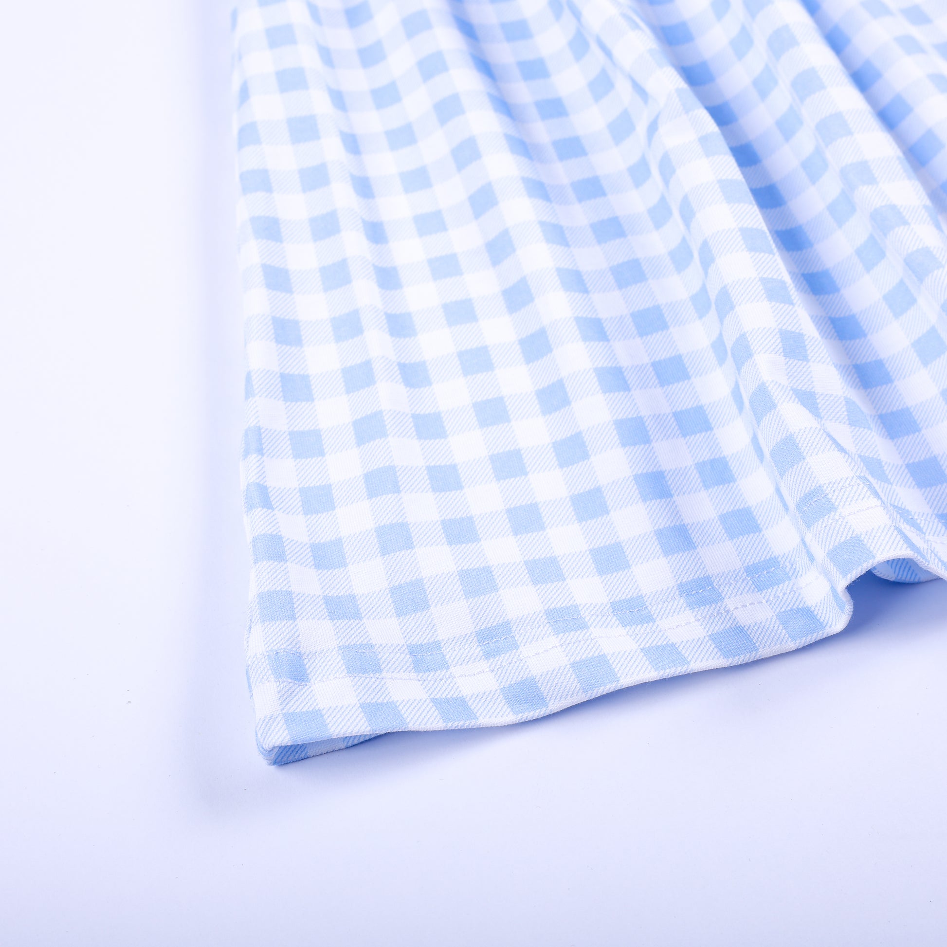 Close-up view of the light blue and white gingham woven fabric hem on a boutique hand-smocked girls dress.