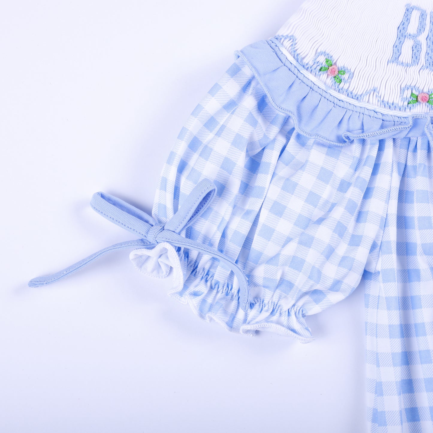 Detailed sleeve view of a light blue gingham smocked dress showing ruffle trim and adjustable fabric tie.