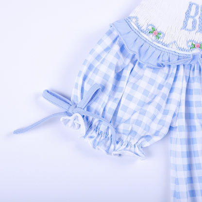 Detailed sleeve view of a light blue gingham smocked dress showing ruffle trim and adjustable fabric tie.