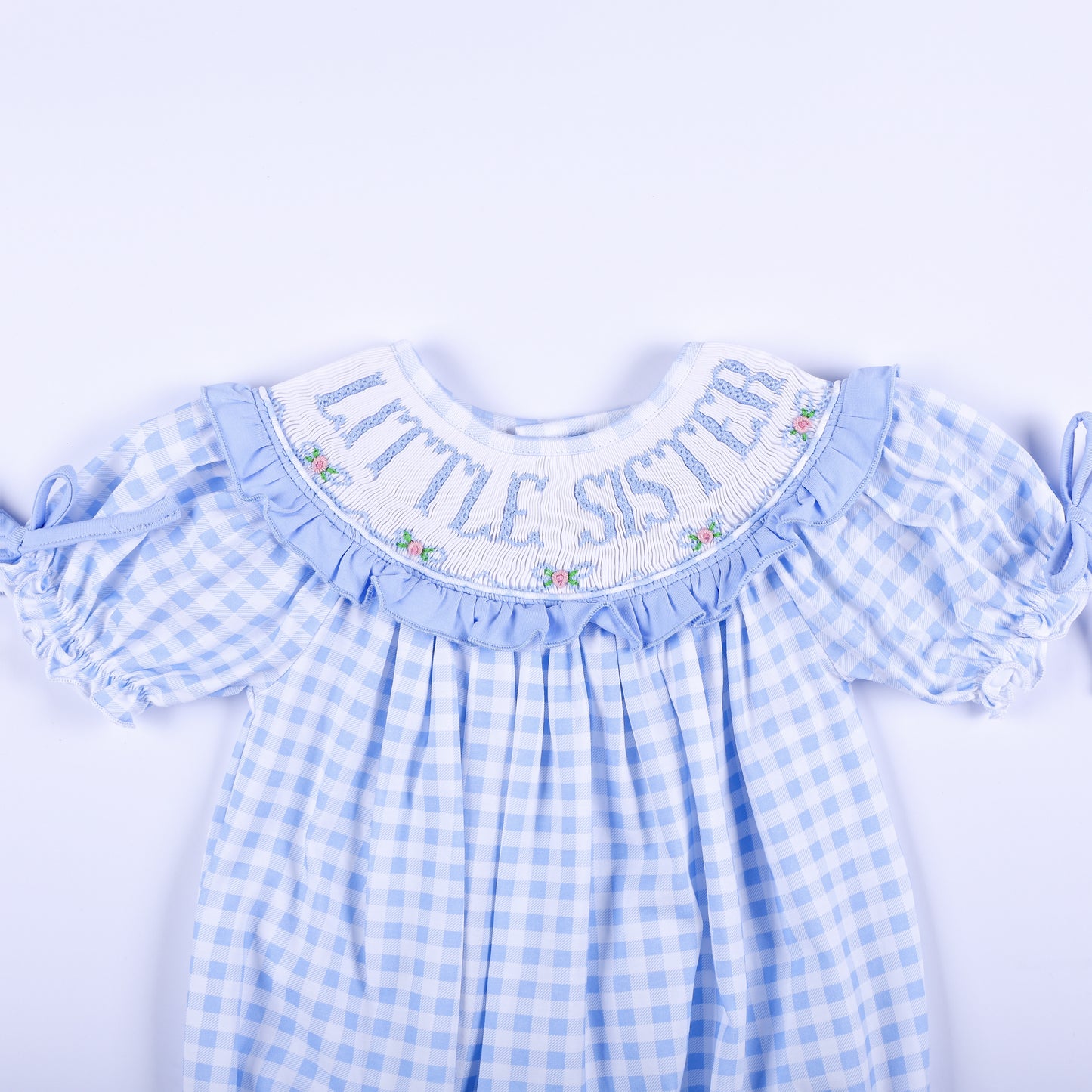 Detailed front collar of blue gingham bubble showing hand-smocked Little Sister text and delicate rose embroidery.