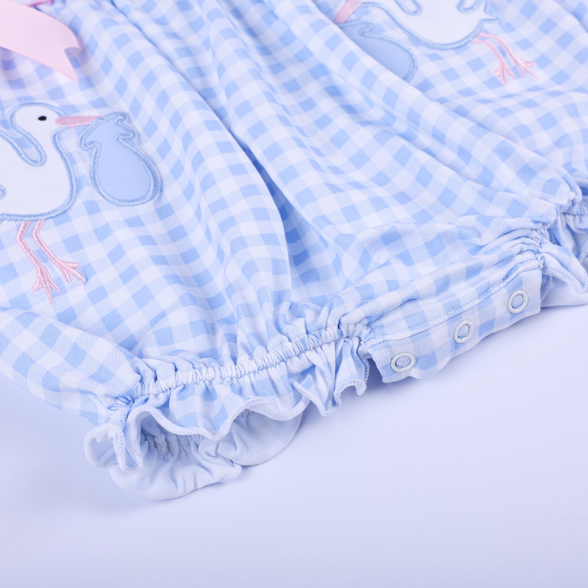 Close-up of the elasticized ruffled leg openings and convenient snap closures on the blue gingham smocked romper.