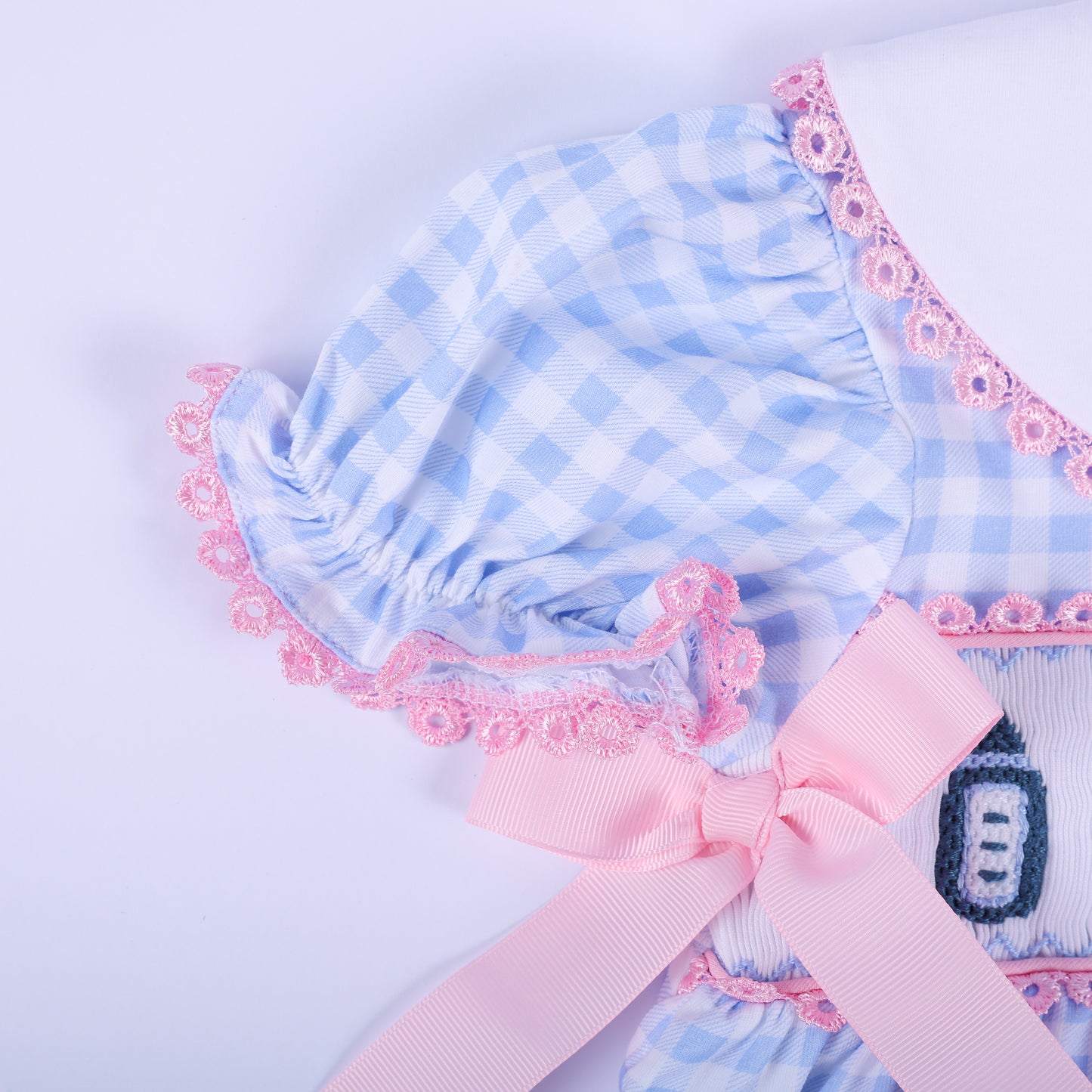 Close-up of the ruffled puff sleeve with pink lace trim and a pink satin waist bow on the blue gingham baby romper.