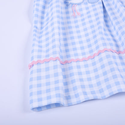Detailed view of the pink rickrack accent trim running along the full hem of light blue gingham check smocked dress.
