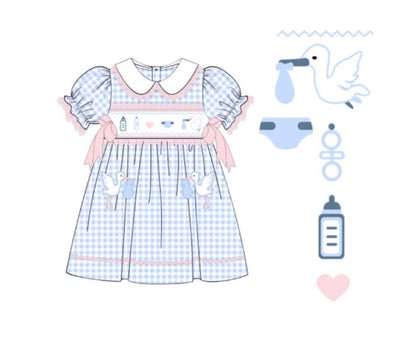 ight blue and white gingham smocked baby dress featuring a white Peter Pan collar, pink bows, and embroidered baby motifs including a stork, bottle, and rattle.