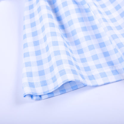 Close-up texture view of blue and white gingham cotton fabric hem on hand-smocked Big Sister baby top.