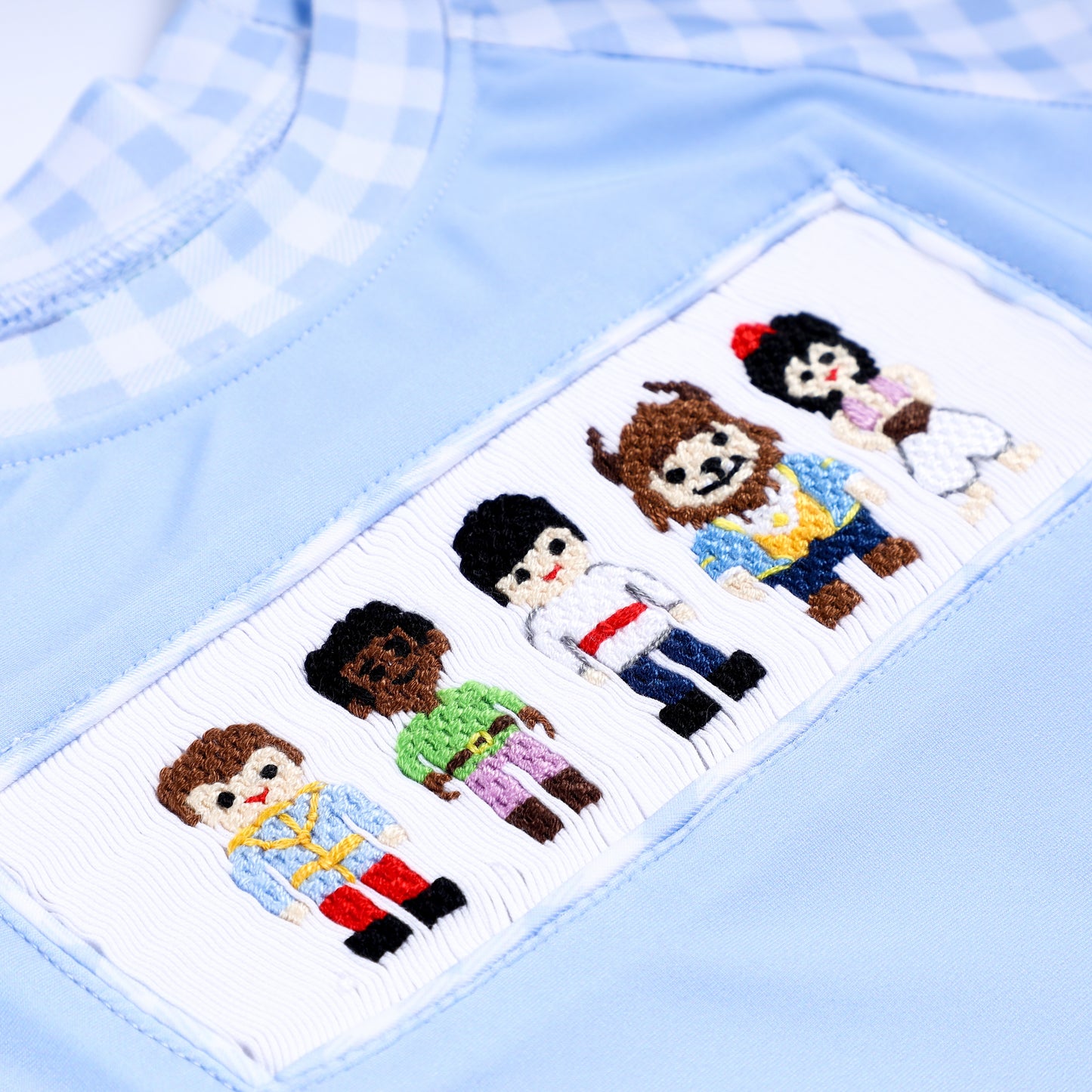 Close up detailed view of hand embroidered prince characters on hand smocked chest panel of boys rash guard swimsuit.