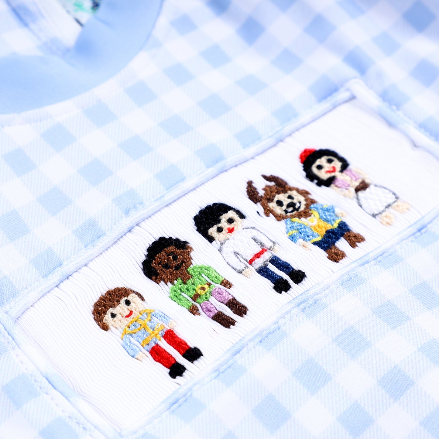 Detailed shot of hand smocked and hand embroidered handsome prince figures on boys blue gingham rash guard swimsuit.