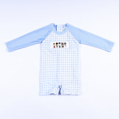 Boys light blue gingham hand smocked handsome prince rash guard swimsuit featuring long sleeves and snap legs.
