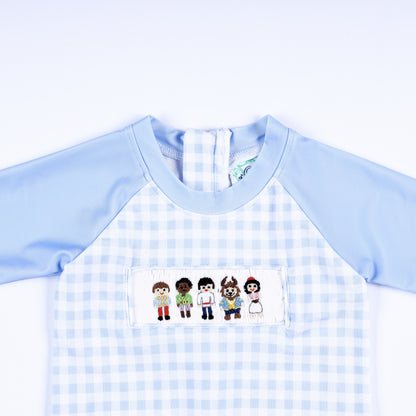 Close-up of boys hand smocked handsome prince rash guard chest featuring detailed hand embroidered fairytale figures.