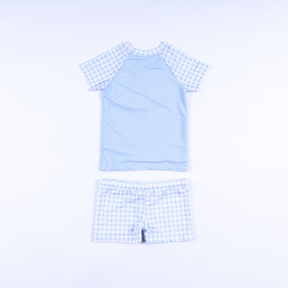 Back view of boys handsome prince hand smocked two piece rash guard swimsuit set with gingham sleeves and swim shorts.