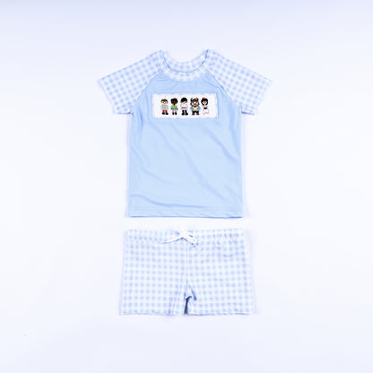 Boys handsome prince hand smocked two piece rash guard swimsuit with light blue top and gingham swim trunks front view.
