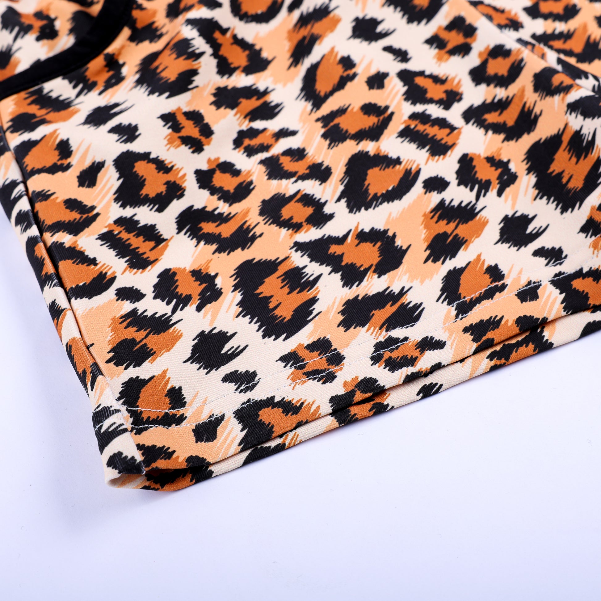 Detailed close-up view of leopard print fabric pattern and stitched bottom hem on boys safari shorts.