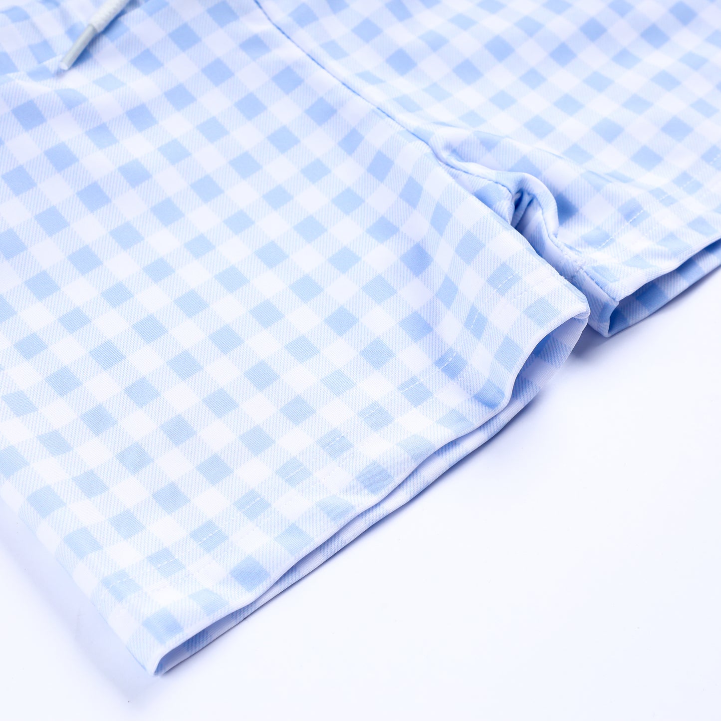 Close up view of light blue and white gingham check pattern fabric on boys handsome prince smocked swim trunks hem.