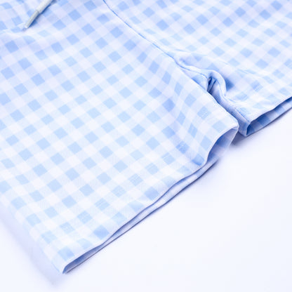 Close up view of light blue and white gingham check pattern fabric on boys handsome prince smocked swim trunks hem.