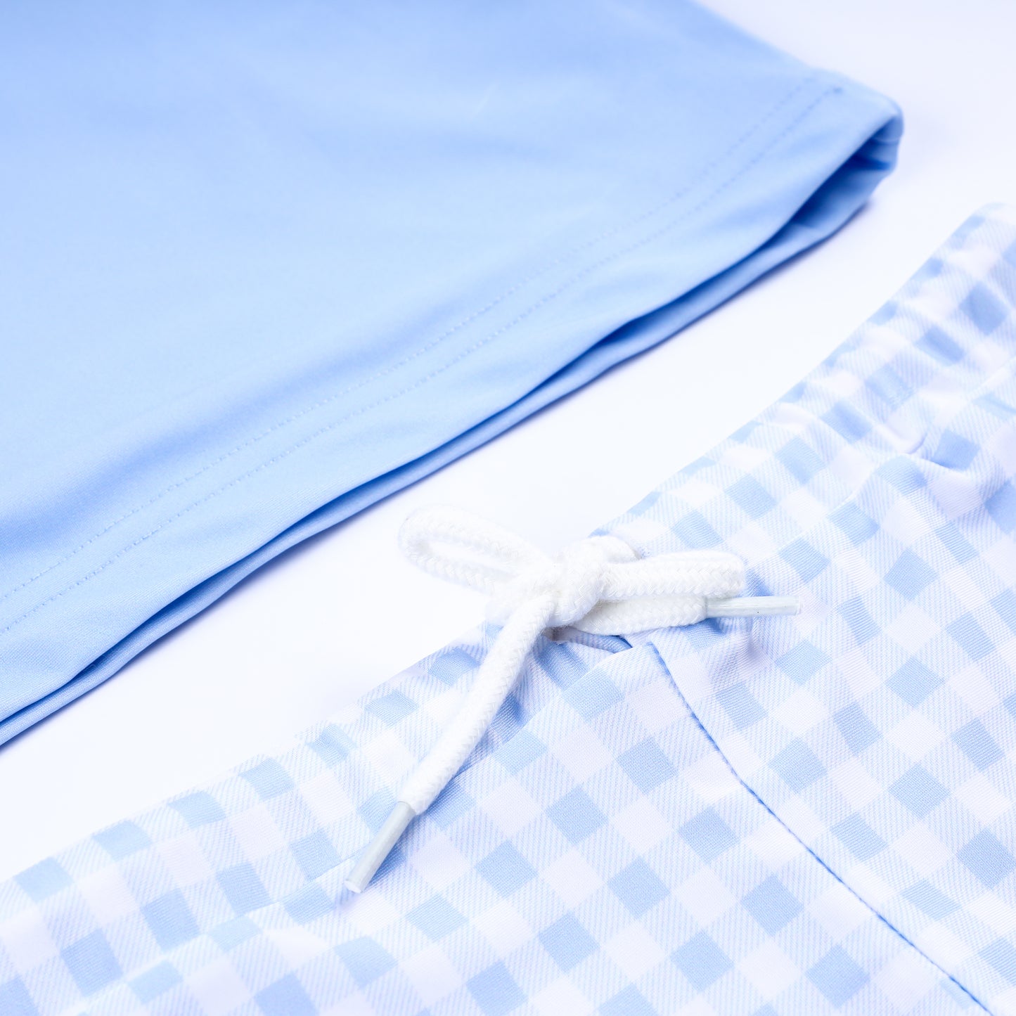 Close up of drawstring waistband on boys blue gingham swim shorts and hem of matching prince hand smocked rash guard.