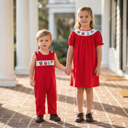 Toddler boy and older sister holding hands in matching red smocked Christmas outfits with holiday embroidery.