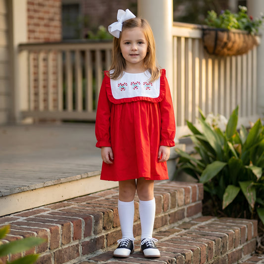 Girl in red Christmas dress with candy cane embroidered bib collar standing outside on brick steps.