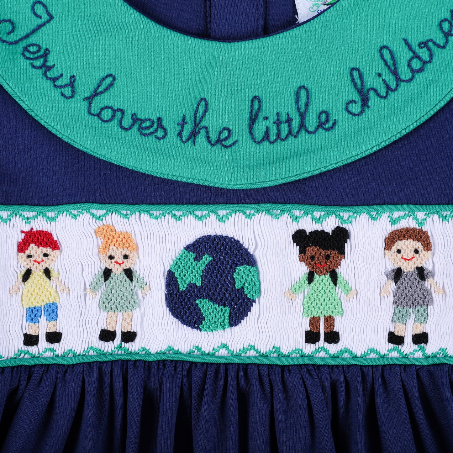 Centered close-up of the navy dress, highlighting the green embroidered collar script and smocked children around a globe.