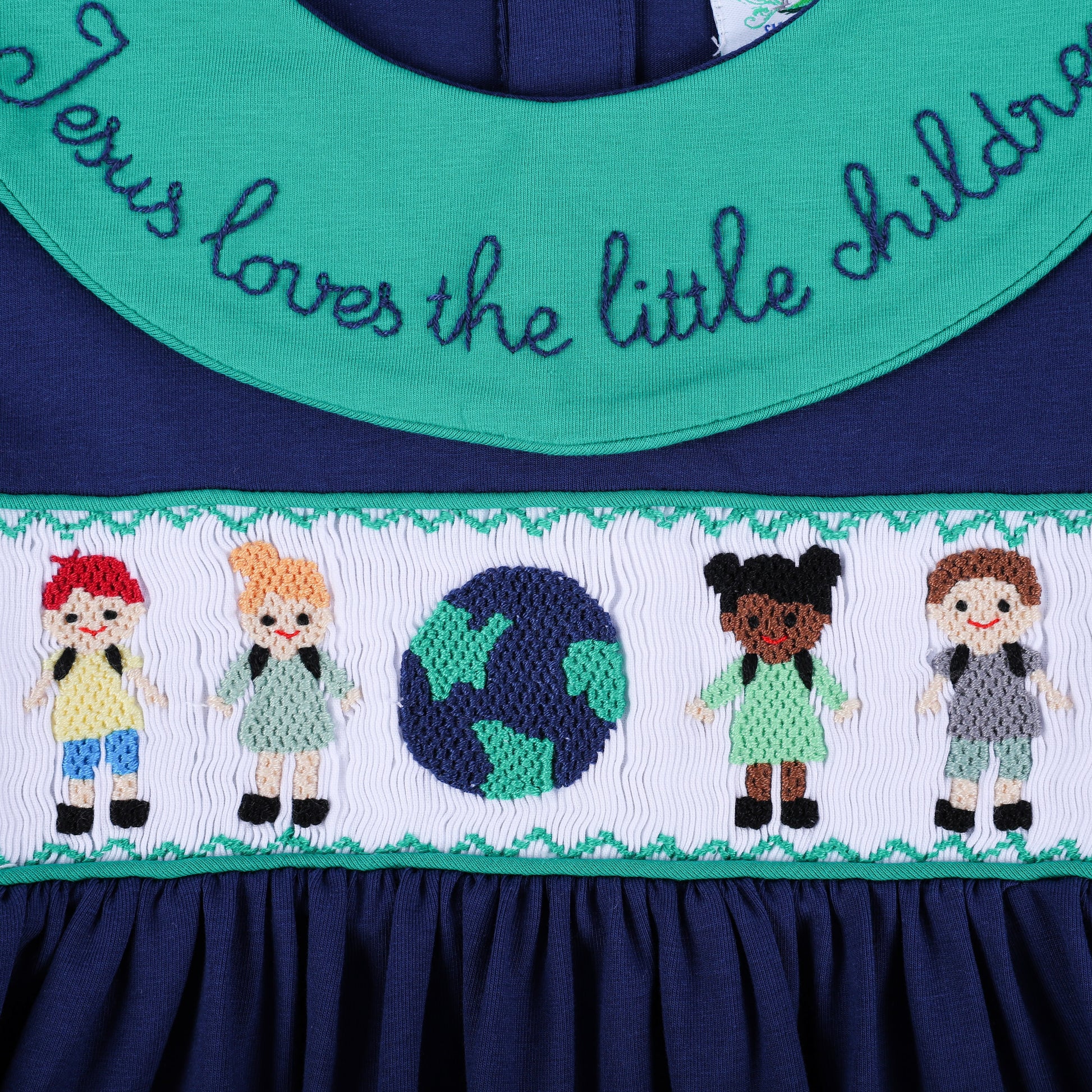 Centered close-up of the navy dress, highlighting the green embroidered collar script and smocked children around a globe.