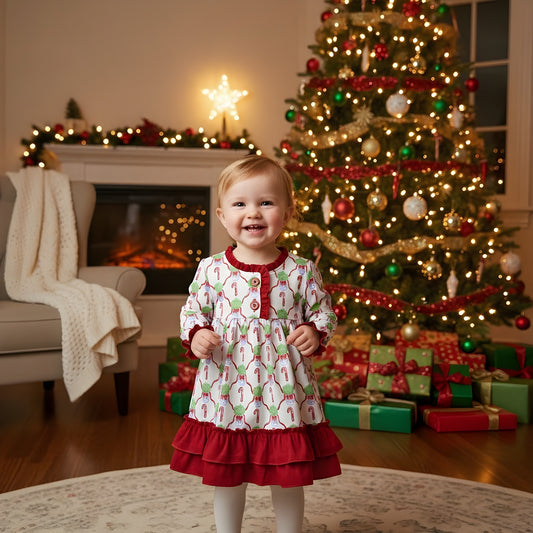 Toddler girl wearing a Christmas white candy cane nightgown with red ruffles standing near a cozy Christmas tree.