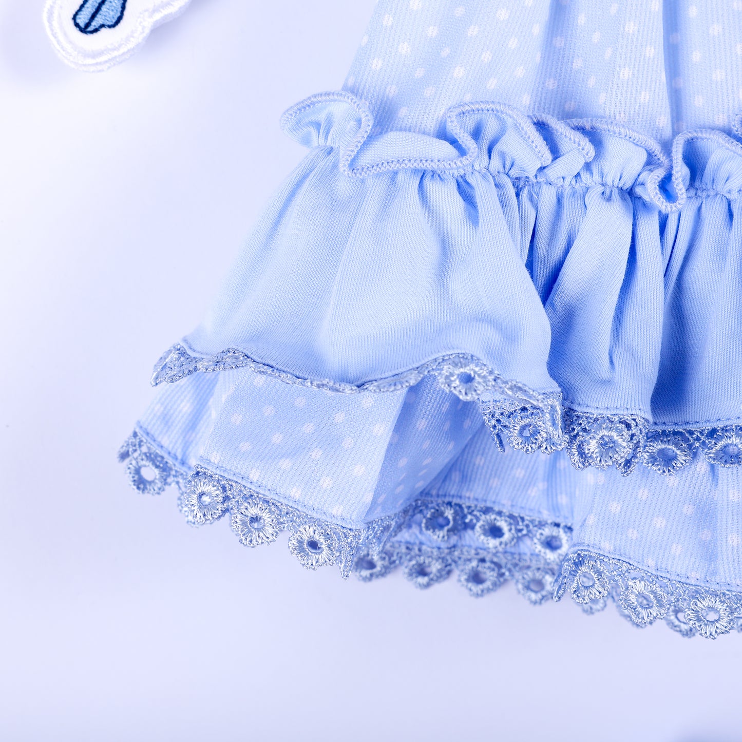 Close-up of tiered ruffle hem with blue lace edging on polka dot Cinderella smocked top for toddlers.