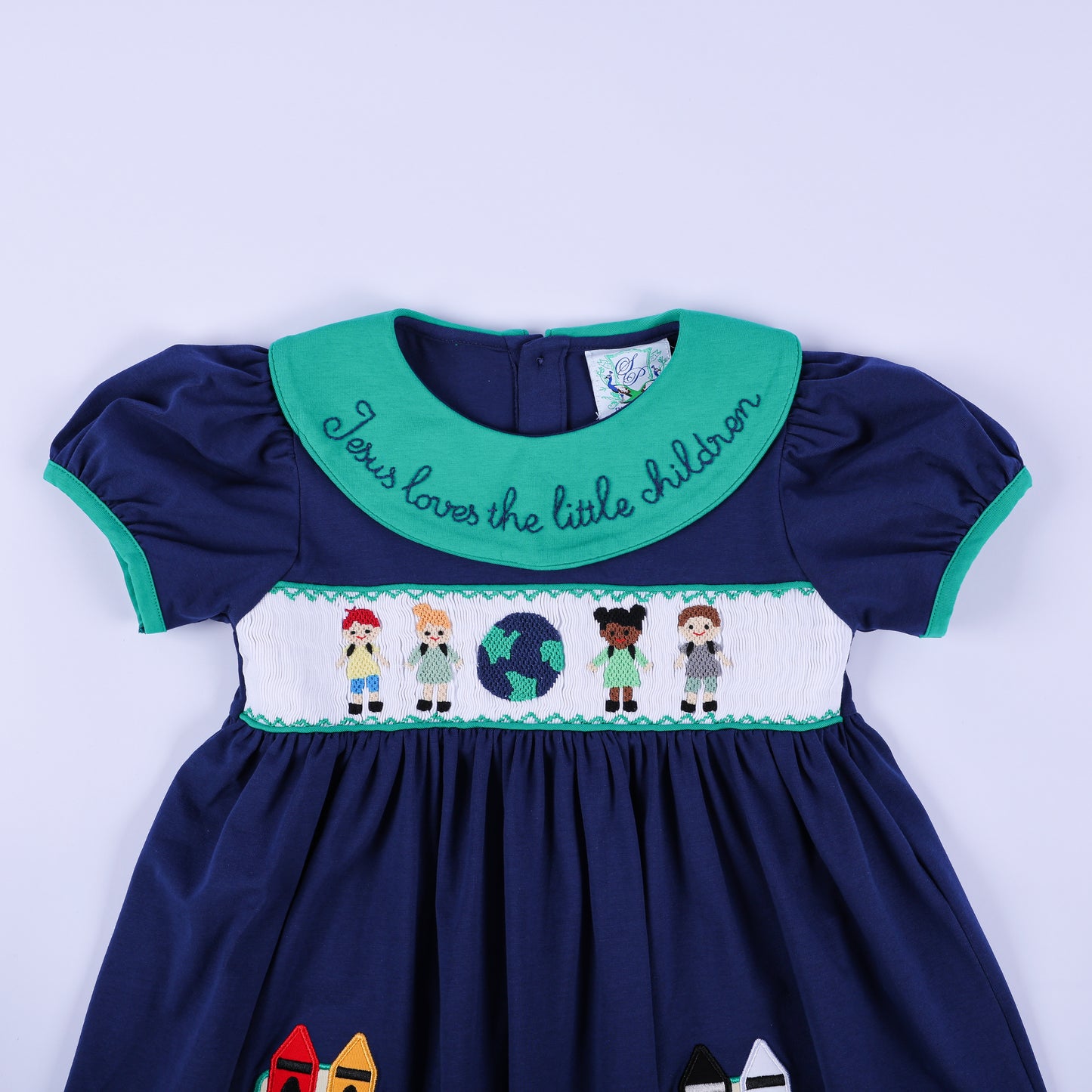 Detailed close-up of the hand-smocked bodice on the navy dress, featuring diverse children and a globe, and the collar embroidery.