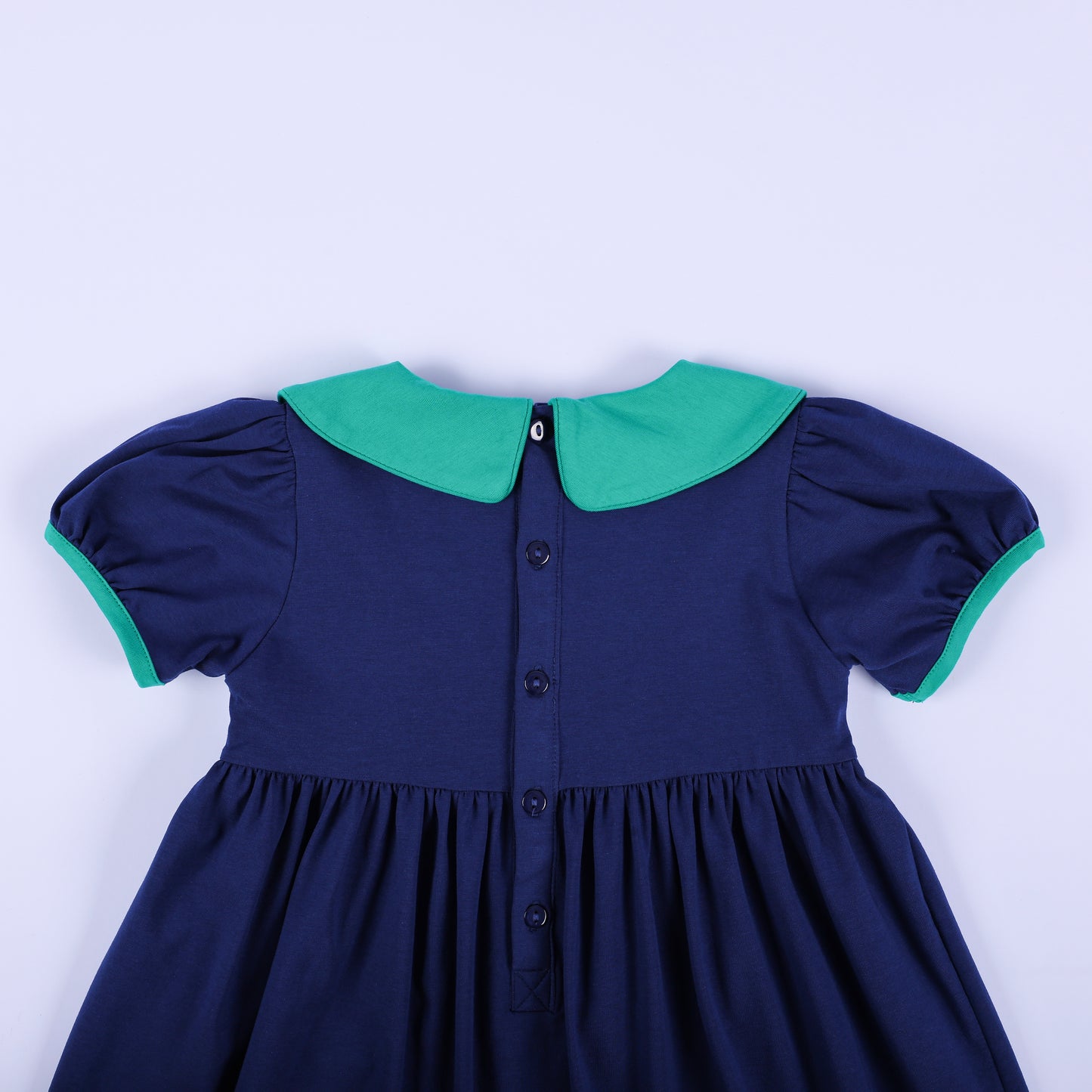 Close-up back view of the navy 'Jesus Loves the Little Children' dress, showing the button closure and solid green collar.