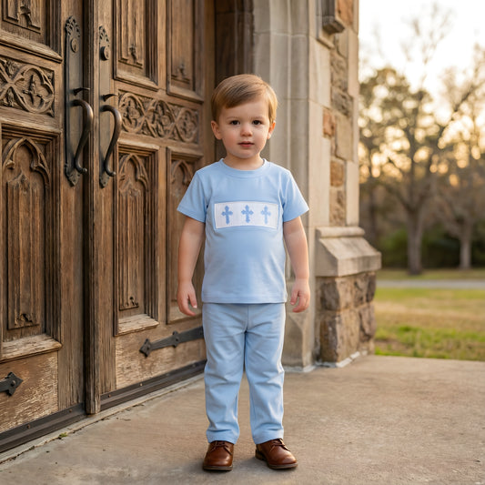 Toddler boy wearing the Hand Smocked Sunday Best blue t-shirt, featuring a white smocked chest panel with three embroidered blue Easter crosses, standing in front of church doors.