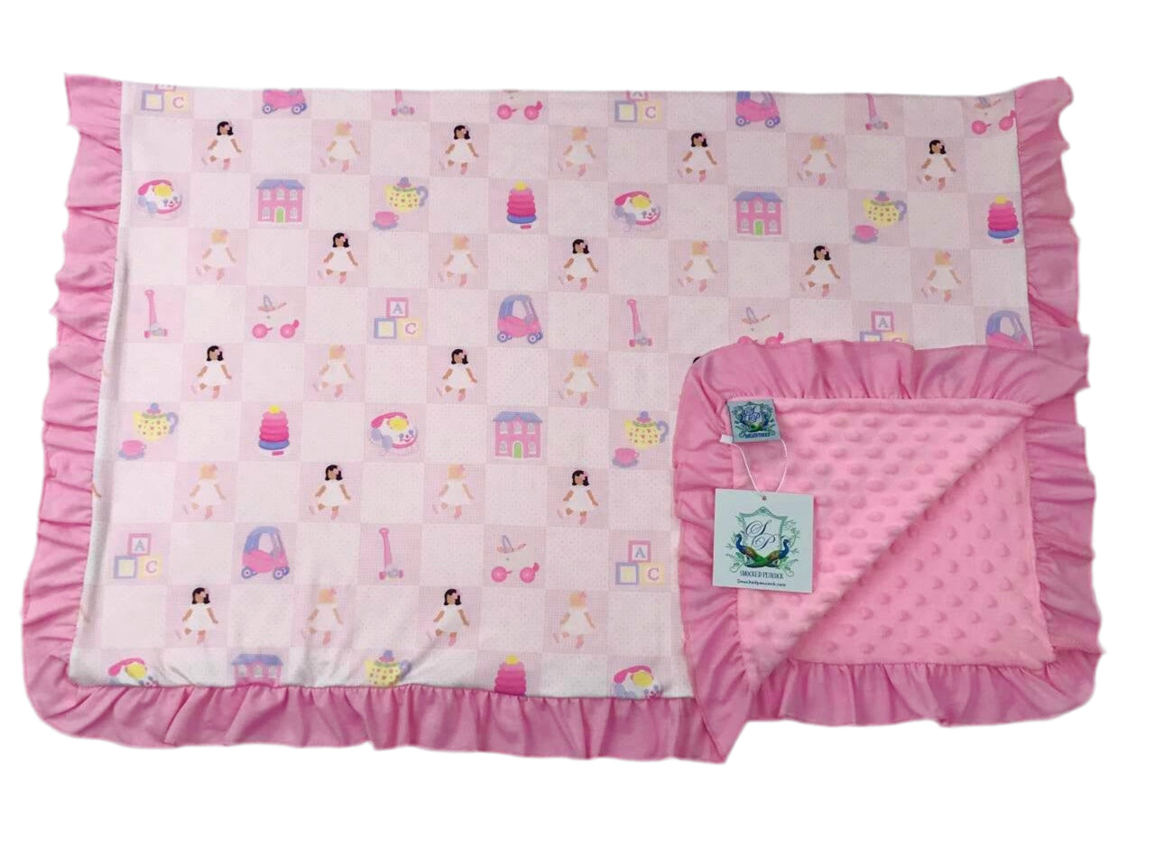 Dolly and Me exclusive print baby blanket featuring a pink doll toy pattern, ruffle trim, and soft minky backing.