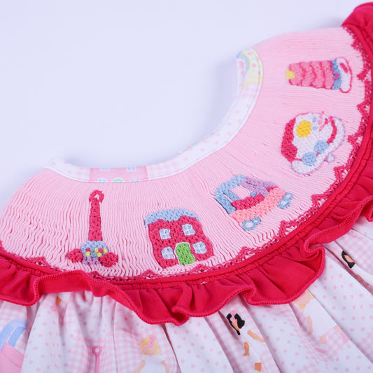 Angled close up of the hand embroidered vintage toys on Dolly & Me pink checkerboard smocked ruffle tunic outfit.