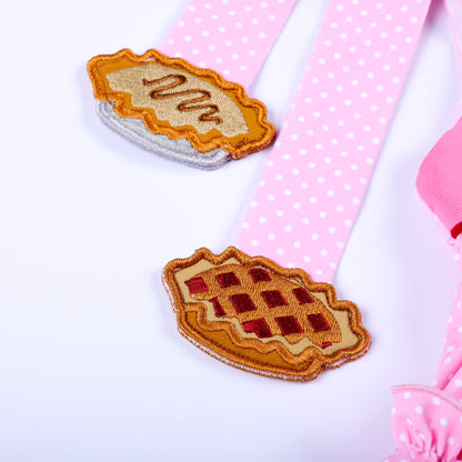Detailed shot of embroidered pie patches on pink polka dot shoulder tie straps for girls bloomer set.