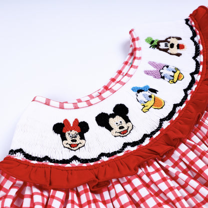 Angled close up of delicate hand embroidered character details on a white smocked neckline with red ruffles.