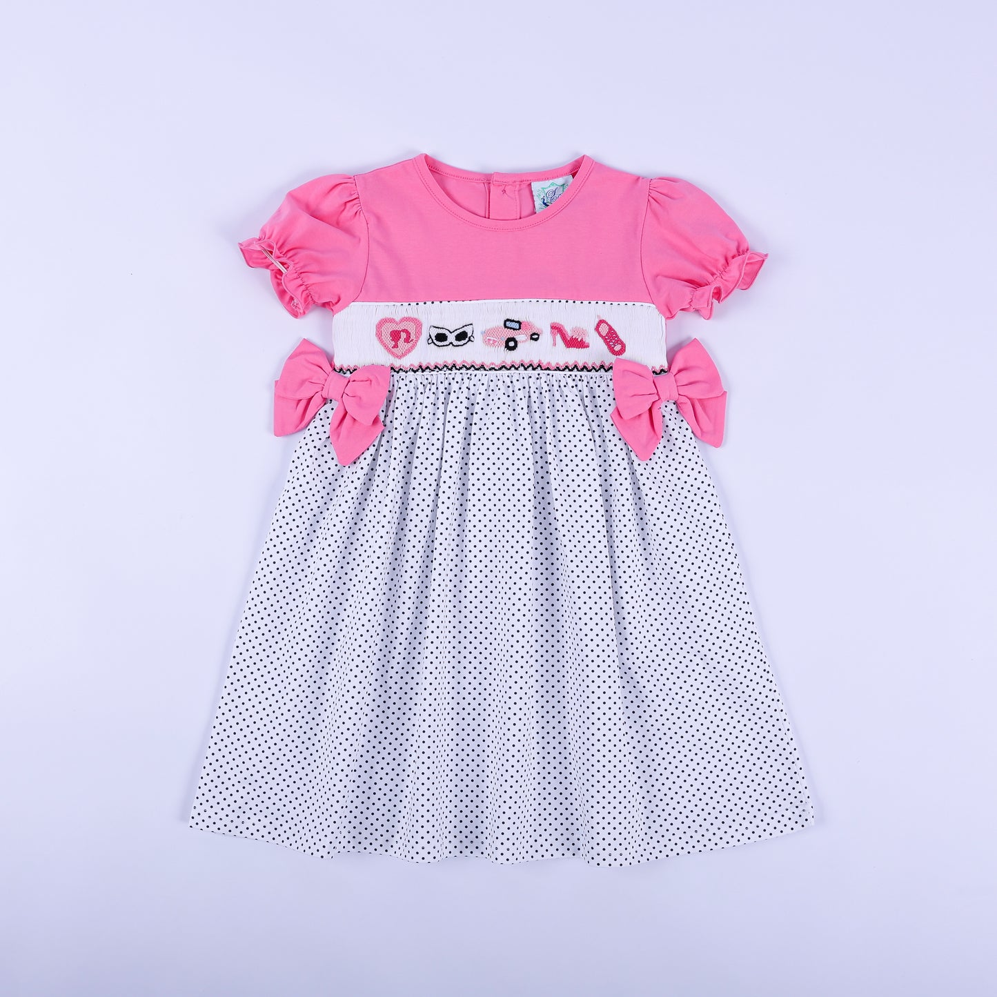 Girls pink polka dot hand smocked dress featuring hand embroidered fashionista motifs and side bows front view.