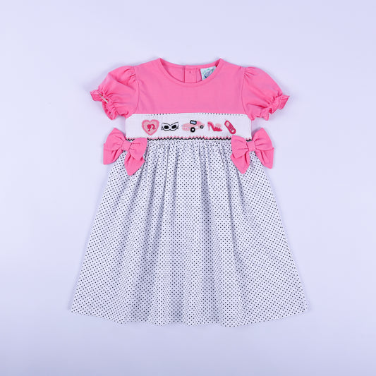 Girls pink polka dot hand smocked dress featuring hand embroidered fashionista motifs and side bows front view.