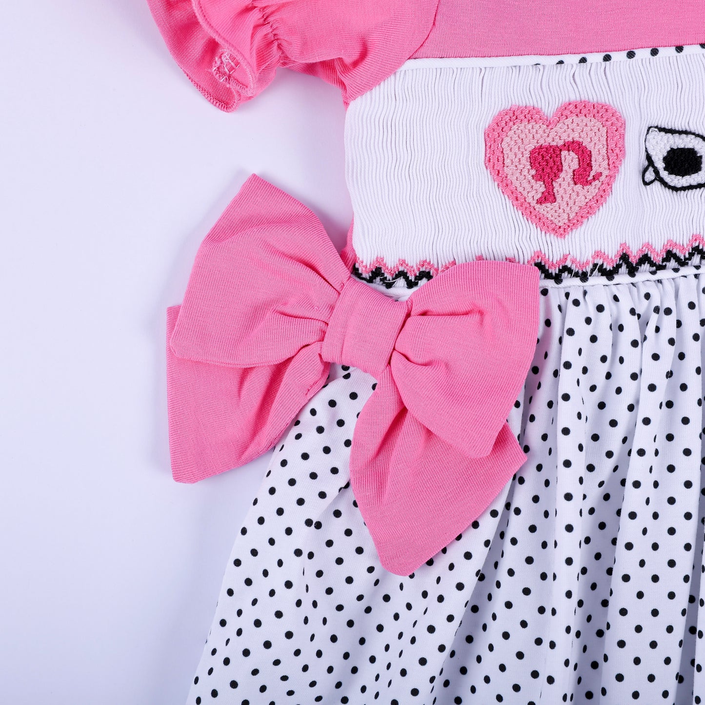 Detail shot of pink side waist bow accent and hand embroidered heart motif on girls polka dot smocked dress.