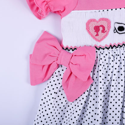Detail shot of pink side waist bow accent and hand embroidered heart motif on girls polka dot smocked dress.