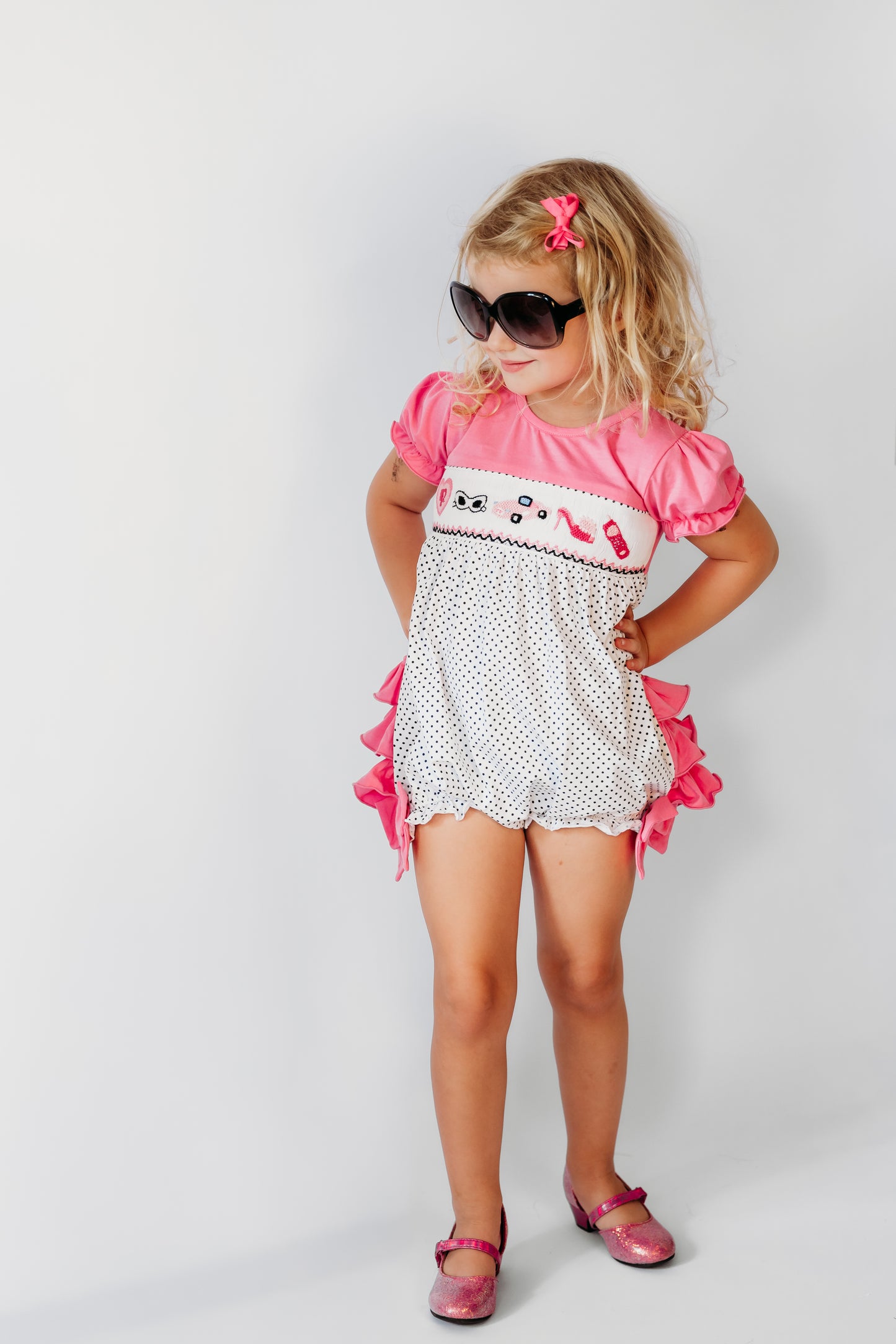 Toddler in sunglasses wearing the pink polka dot hand-smocked fashionista embroidered bubble romper.