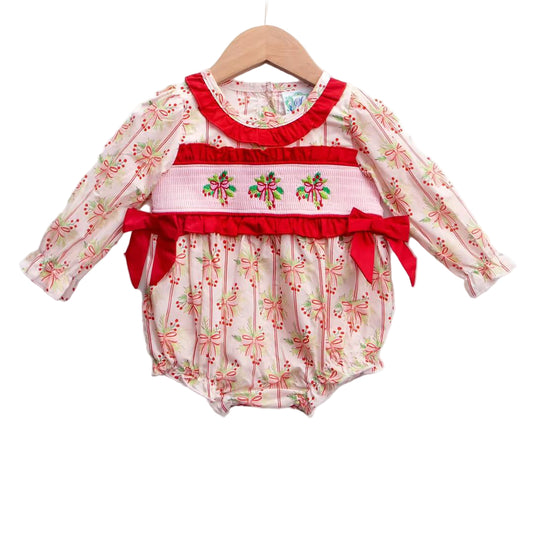 Baby girl's smocked bubble romper with holly berry and bow print, red smocking, and festive side bows.