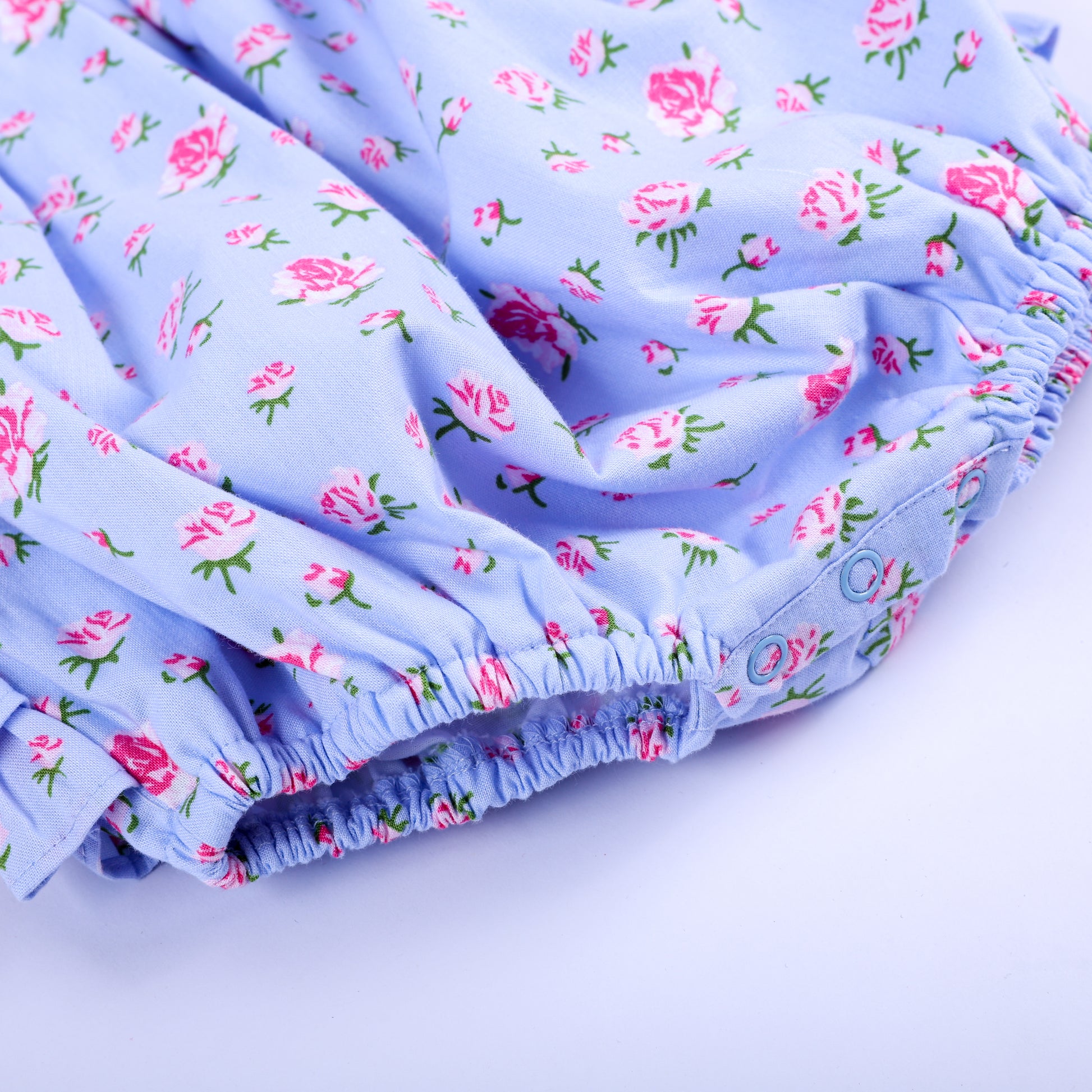 Bottom snap closure and elastic leg gathering on light blue floral smocked baby bubble for easy changes.