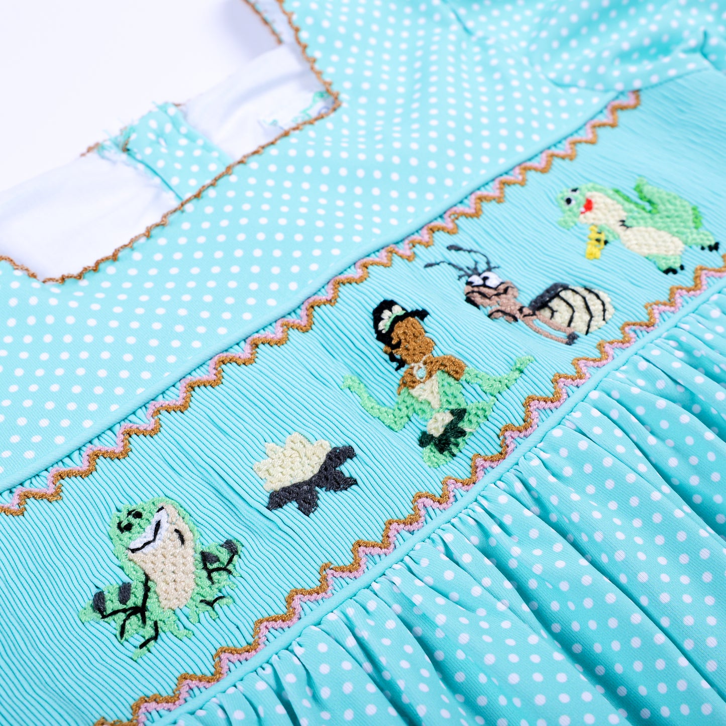 Detailed view of hand embroidered frog princess and lotus characters on aqua hand smocked girls dress.