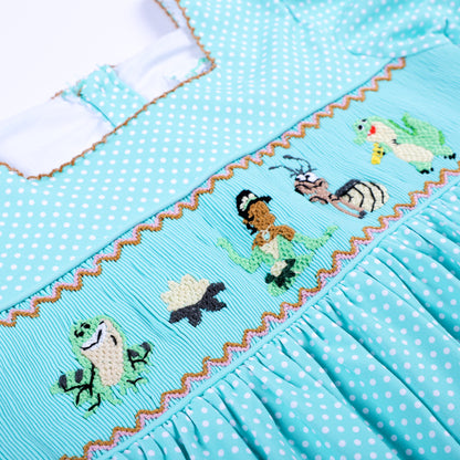Detailed view of hand embroidered frog princess and lotus characters on aqua hand smocked girls dress.