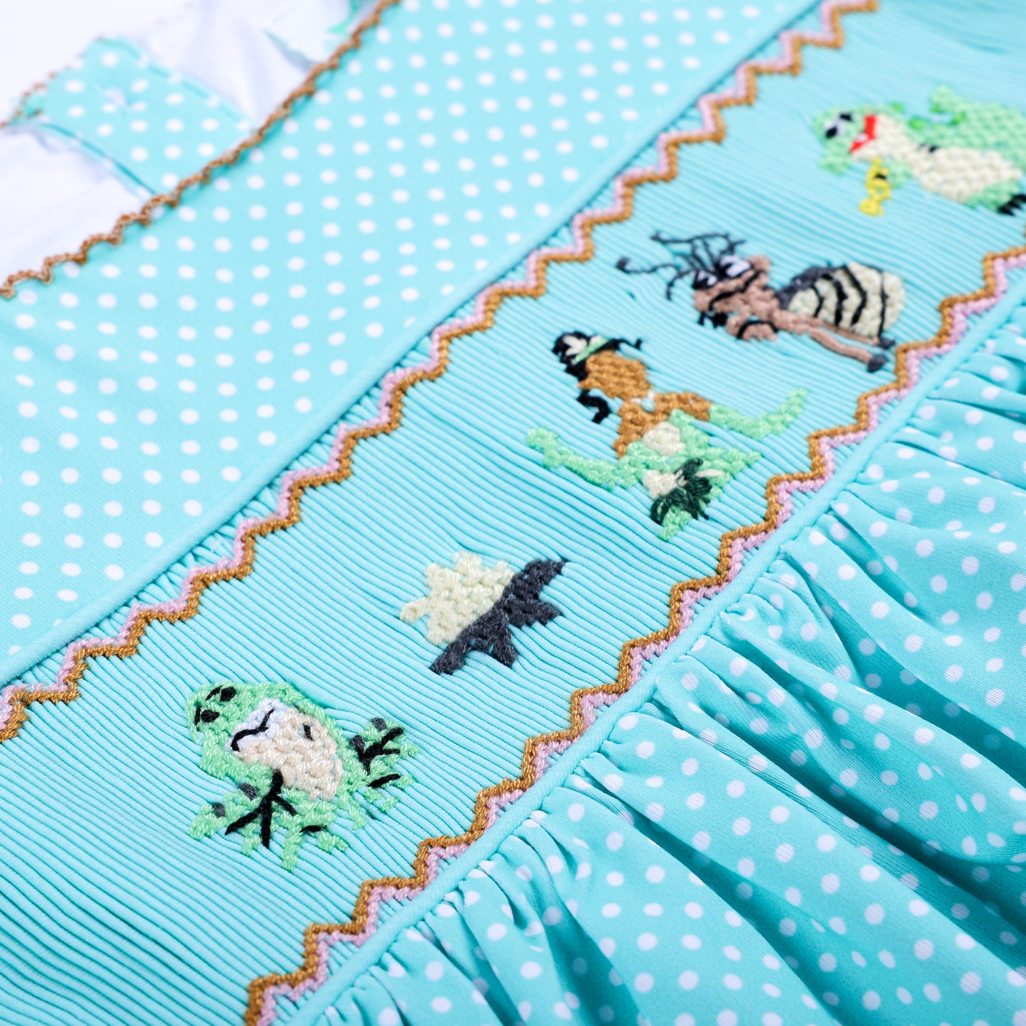 Detailed close-up of hand-smocked and hand-embroidered Frog Princess lotus design on aqua polka dot top.