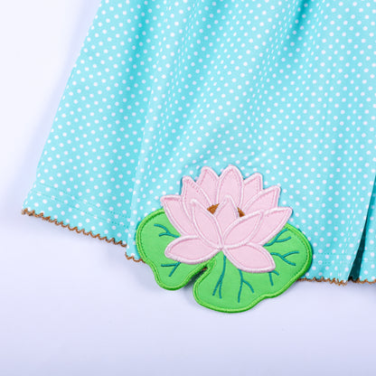 Close-up view of pink lotus flower applique hand sewn on hem of aqua polka dot smocked dress for girls.