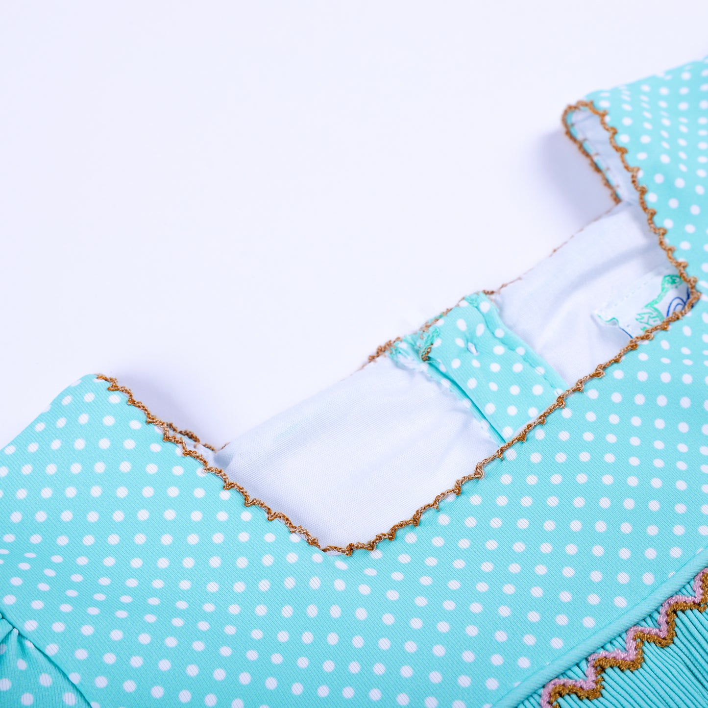 Detailed close-up of square neckline with brown picot stitch trim on girls frog princess smocked dress.