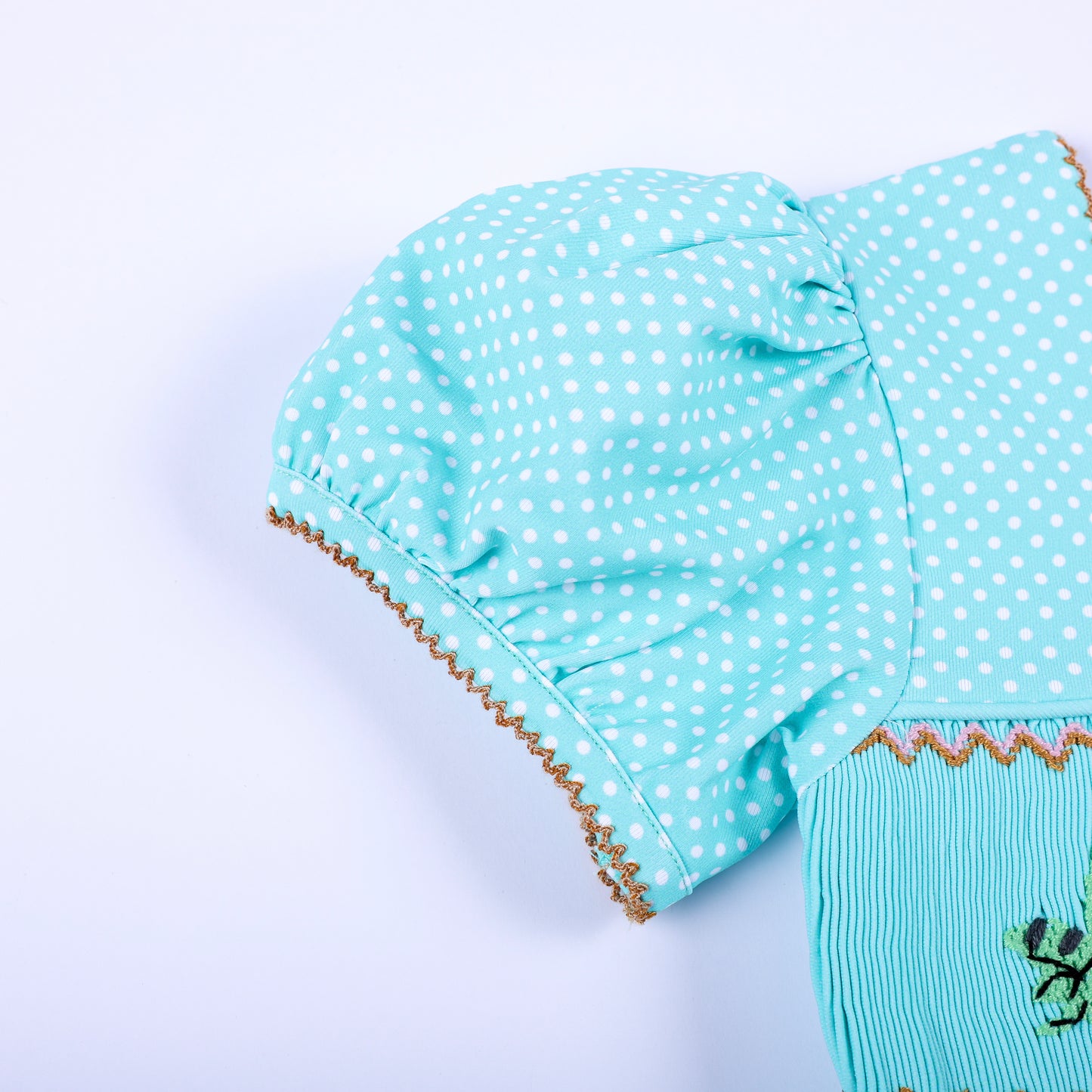 Detail view of puff sleeve on aqua polka dot smocked girls dress featuring brown picot embroidery trim.