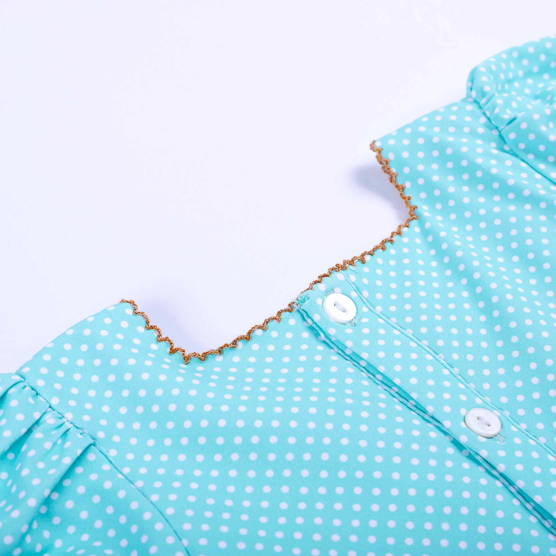 Detailed close-up of back button closure on aqua polka dot hand-smocked top with gold picot trim detail.