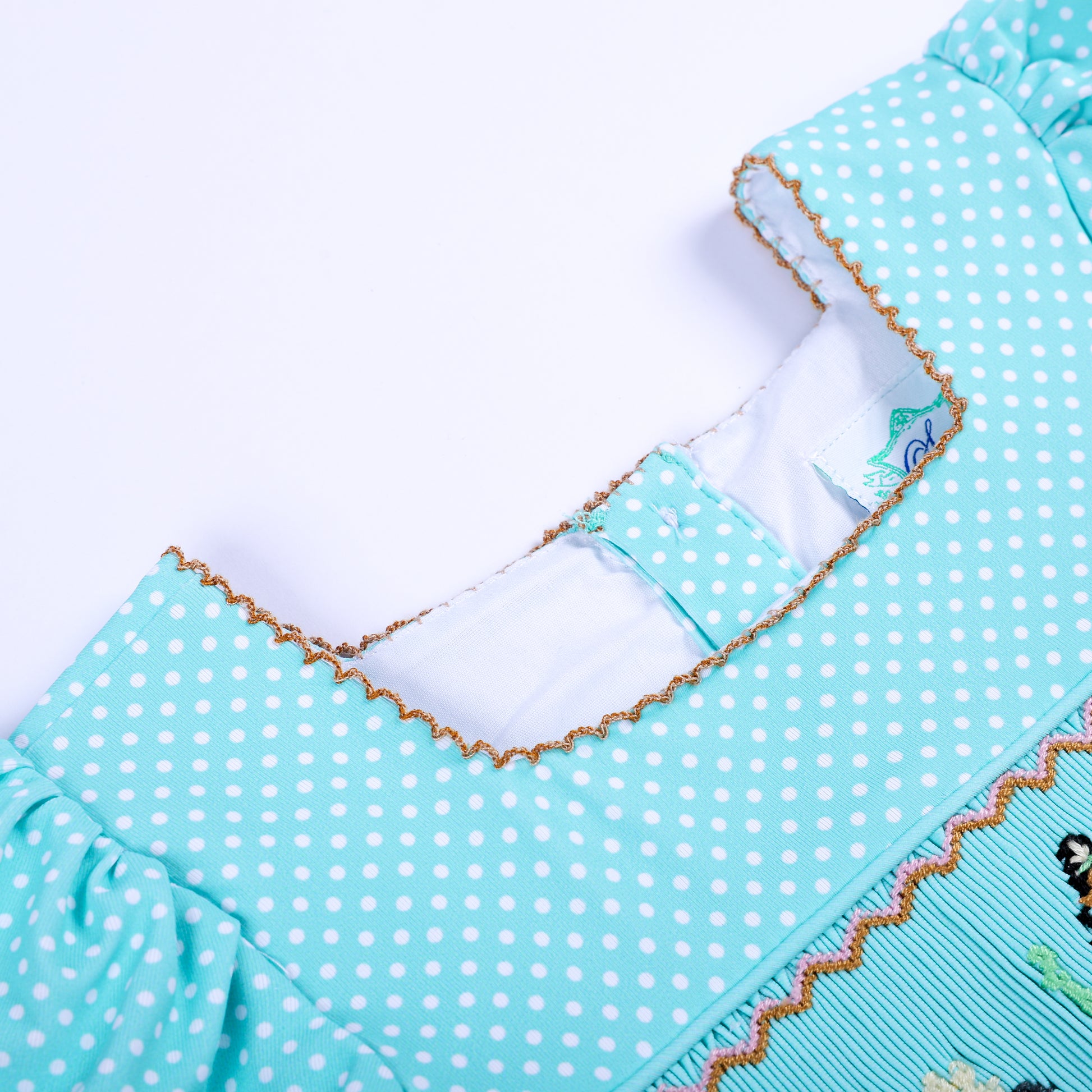 Close-up of front square neckline with gold scallop picot edging on aqua polka dot smocked boutique shirt.